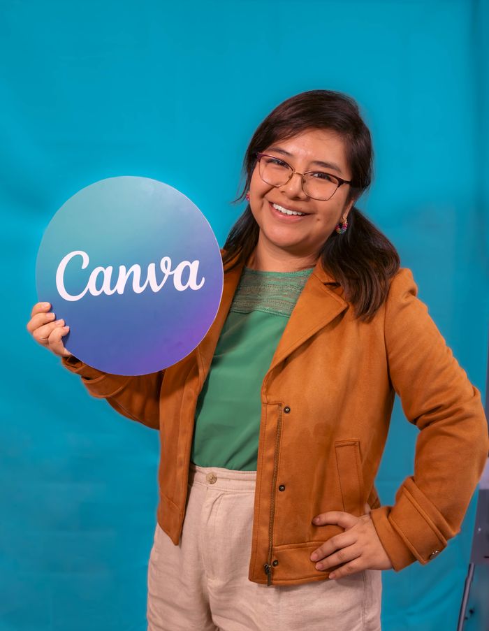 project-02-d A smiling woman in a casual outfit holds a Canva sign, posing confidently against a vibrant blue backdrop.