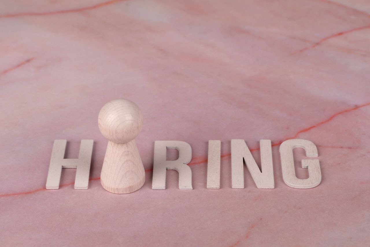 services-01 Wooden letters spelling hiring on pink marble background with a peg.